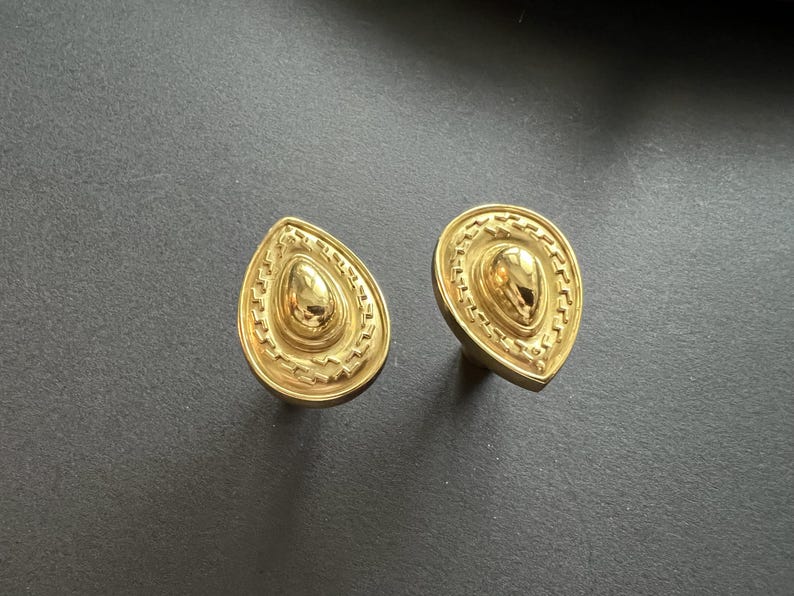 May include: A pair of gold teardrop-shaped earrings with intricate embossed designs.