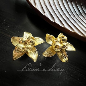 Peut inclure: Une paire de boucles d'oreilles dorées en forme de fleur avec un groupe de perles rondes dorées au centre.
