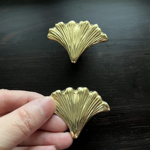Op de afbeelding: Twee gouden metalen kastknoppen in de vorm van ginkgo bladeren.