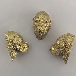May include: Three gold-colored gorilla head sculptures. The sculptures are detailed and realistic, with fur and facial features.