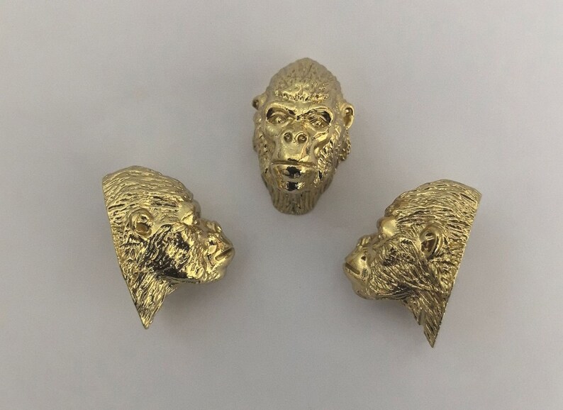 May include: Three gold-colored gorilla head sculptures. The sculptures are detailed and realistic, with fur and facial features.