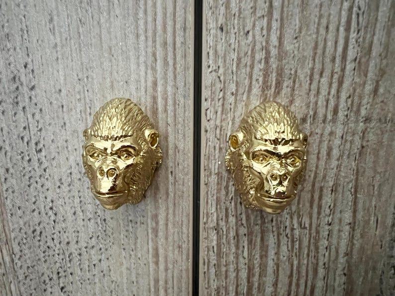 May include: Two gold-colored gorilla head cabinet knobs. The knobs are detailed with a textured finish and have a realistic gorilla face.