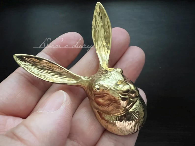 K&ouml;nnte beinhalten: Eine goldfarbene Kaninchenkopfskulptur mit detaillierten Merkmalen. Die Skulptur ist aus Metall und hat ein realistisches Aussehen.