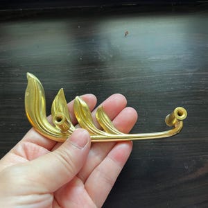May include: Gold-toned metal cabinet pull with a leaf design. The pull has two holes for mounting.