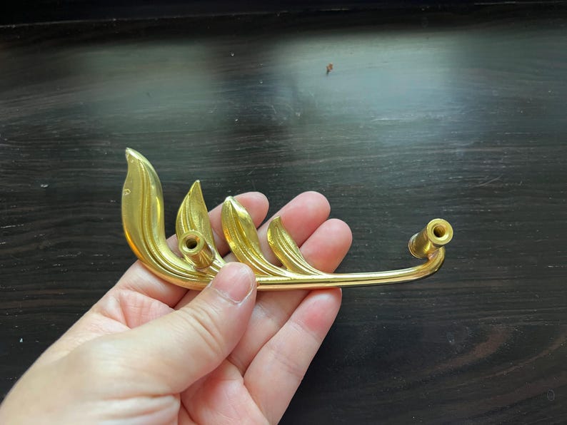 May include: Gold-toned metal cabinet pull with a leaf design. The pull has two holes for mounting.
