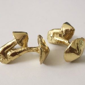 May include: A pair of gold-toned cufflinks shaped like mushrooms. Each cufflink has a detailed, textured design.