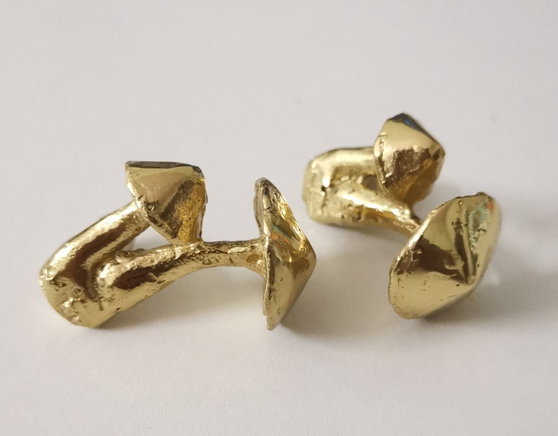 May include: A pair of gold-toned cufflinks shaped like mushrooms. Each cufflink has a detailed, textured design.