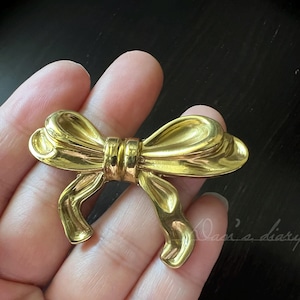 May include: A gold-toned bow-shaped brooch. The bow is made of smooth metal and has a shiny finish.