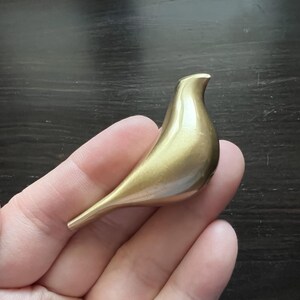 K&ouml;nnte beinhalten: Eine goldfarbene Vogelfigur aus Metall. Der Vogel ist stilisiert und hat eine glatte, abgerundete Form.