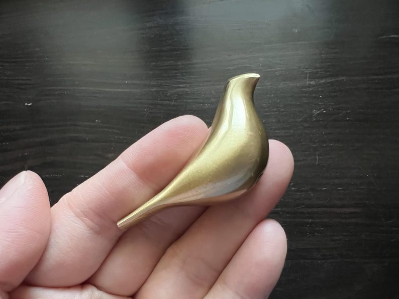 K&ouml;nnte beinhalten: Eine goldfarbene Vogelfigur aus Metall. Der Vogel ist stilisiert und hat eine glatte, abgerundete Form.