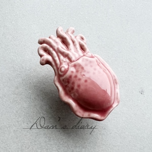 以下が含まれることがあります： 触手のあるイカの形をしたピンクのセラミック製のキャビネットノブです。