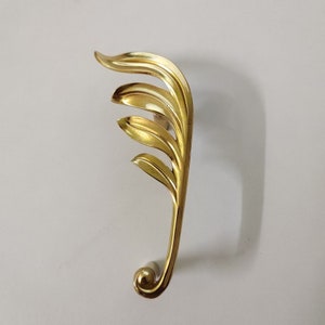 May include: A gold-toned door handle with a leaf design. The handle is curved and has a rounded end.