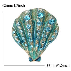 May include: A seashell brooch, measuring 42mm wide and 37mm tall, with a teal and gold finish. The brooch is embellished with numerous round, light blue rhinestones, adding sparkle to the design.