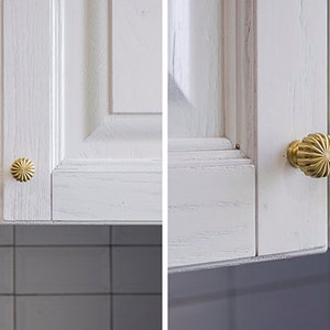 Puede incluir: Dos puertas de armario blancas con pomos dorados. Los pomos tienen un dise&ntilde;o decorativo festoneado.