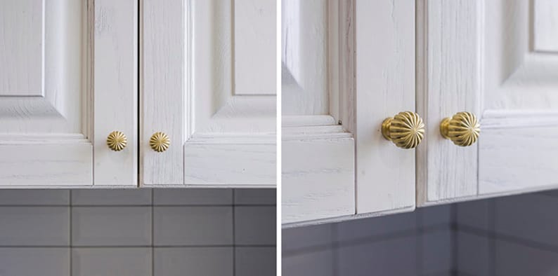 Puede incluir: Dos puertas de armario blancas con pomos dorados. Los pomos tienen un dise&ntilde;o decorativo festoneado.