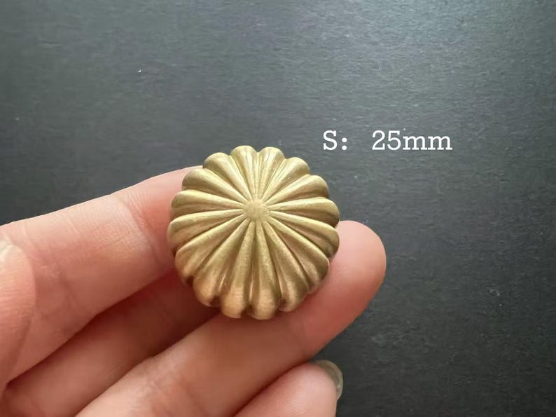 Puede incluir: Un pomo decorativo redondo de color dorado con un dise&ntilde;o de rayos de sol. El pomo mide 25 mm de di&aacute;metro. S: 25mm