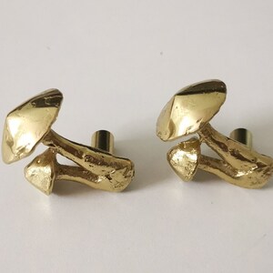 May include: Two gold mushroom-shaped cabinet knobs. The knobs are made of a textured metal and have a realistic mushroom design.