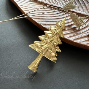 Pode incluir: Um enfeite de árvore de Natal de metal dourado em forma de pinheiro. O enfeite é detalhado com uma superfície texturizada e está sobre uma superfície de madeira.