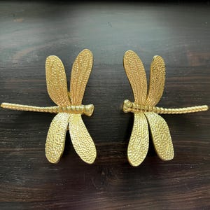 May include: Two gold-coloured dragonfly drawer pulls with intricate details.