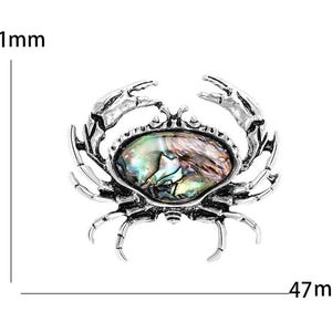 K&ouml;nnte beinhalten: Silberfarbene Krabbenbrosche mit einem ovalen, schillernden Stein in der Mitte. Die Brosche ist etwa 47 mm breit und 41 mm hoch. Die Krallen und Beine der Krabbe sind detailliert gestaltet.