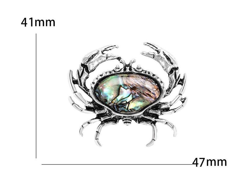 K&ouml;nnte beinhalten: Silberfarbene Krabbenbrosche mit einem ovalen, schillernden Stein in der Mitte. Die Brosche ist etwa 47 mm breit und 41 mm hoch. Die Krallen und Beine der Krabbe sind detailliert gestaltet.
