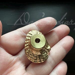 May include: A gold-colored metal cabinet knob with a decorative, textured design. The knob has a round, flat top with a small hole in the center.