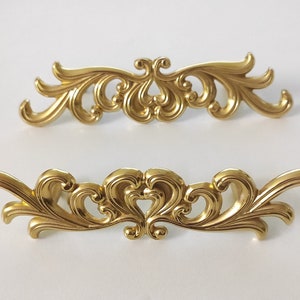 May include: Two ornate gold-toned metal drawer pulls with a decorative scroll design.