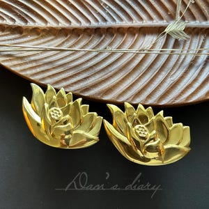 May include: A pair of gold-tone lotus flower earrings. The earrings are detailed with a raised center and petals.