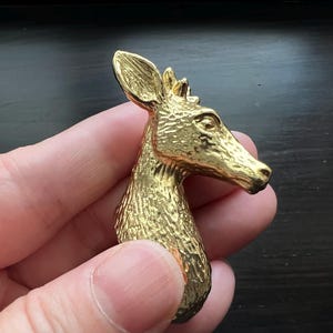 以下が含まれることがあります： テクスチャ加工された表面を持つ金色の鹿の頭部のブローチ