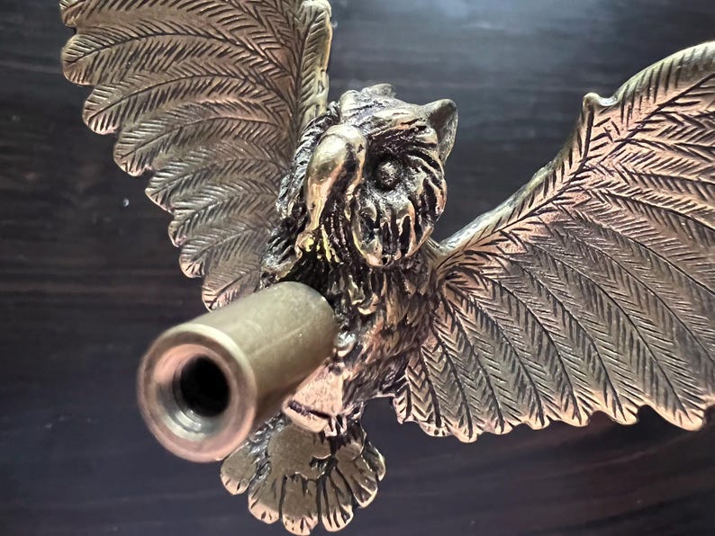 K&ouml;nnte beinhalten: Eine detaillierte Eulen-Skulptur aus Messing mit ausgebreiteten Fl&uuml;geln und einem zylindrischen Lauf, der aus der Brust ragt. Die Eule ist aufwendig mit strukturierten Federn und einem fokussierten Blick versehen.
