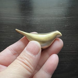 K&ouml;nnte beinhalten: Eine goldfarbene Vogelfigur aus Metall. Der Vogel ist stilisiert und hat eine glatte, abgerundete Form.