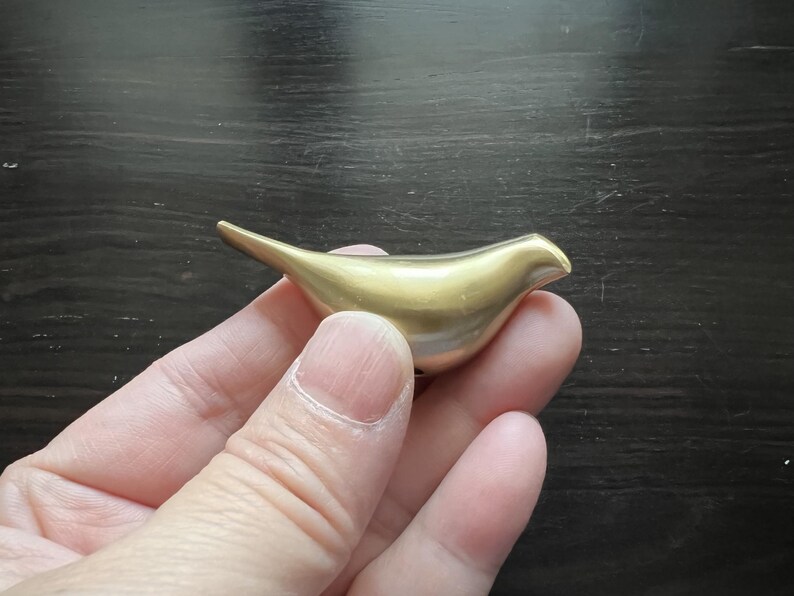 K&ouml;nnte beinhalten: Eine goldfarbene Vogelfigur aus Metall. Der Vogel ist stilisiert und hat eine glatte, abgerundete Form.