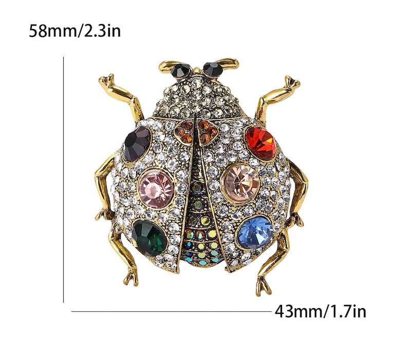 May include: A gold-coloured ladybug brooch, 5.8 cm long and 4.3 cm wide, adorned with clear and colourful gemstones. The brooch has a detailed design with multiple coloured gems and a gold-coloured metal frame.