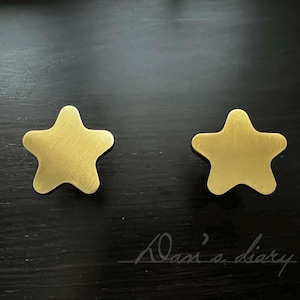 May include: Two gold-colored star-shaped objects. The stars have a matte finish and are placed on a dark surface. The image includes the handwritten text "Dan's diary" in the bottom right corner.