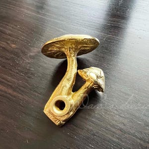 May include: Gold-toned metal mushroom-shaped door knob with a detailed design. The knob is attached to a round base.