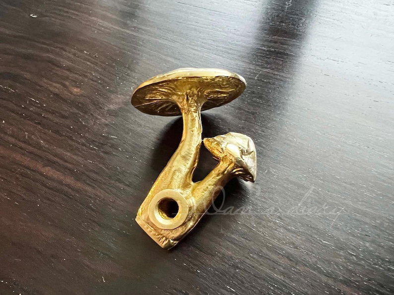 May include: Gold-toned metal mushroom-shaped door knob with a detailed design. The knob is attached to a round base.