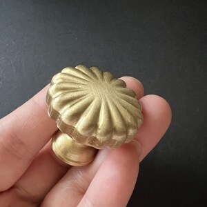 Puede incluir: Un pomo de armario de metal dorado con un dise&ntilde;o acanalado y festoneado. El pomo tiene una base redonda y una parte superior decorativa elevada.