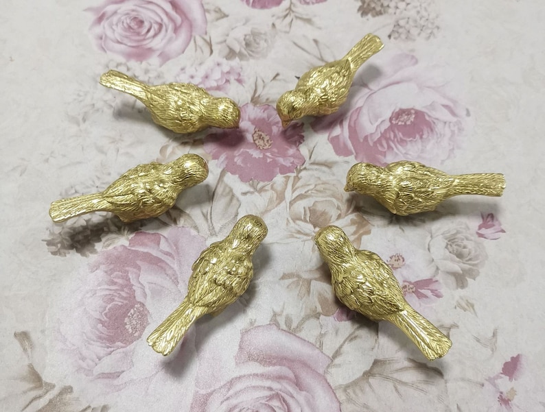 Puede incluir: Seis figuritas de p&aacute;jaros de color dorado dispuestas en c&iacute;rculo sobre un fondo floral rosa.