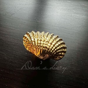 May include: A gold-colored seashell-shaped cabinet knob.