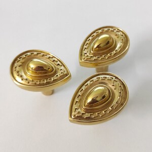 May include: Three gold-toned teardrop-shaped cabinet knobs with a decorative, raised, concentric circle design.