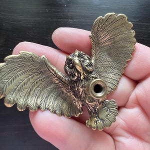 K&ouml;nnte beinhalten: Detaillierte Eulenfigur aus Messing mit ausgebreiteten Fl&uuml;geln. Die Eule hat aufwendige Federdetails und eine kreisf&ouml;rmige &Ouml;ffnung in der Brust. Die Fl&uuml;gel sind weit ausgebreitet.