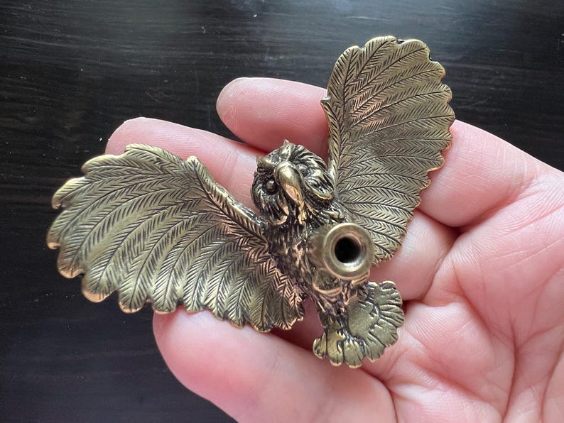 K&ouml;nnte beinhalten: Detaillierte Eulenfigur aus Messing mit ausgebreiteten Fl&uuml;geln. Die Eule hat aufwendige Federdetails und eine kreisf&ouml;rmige &Ouml;ffnung in der Brust. Die Fl&uuml;gel sind weit ausgebreitet.