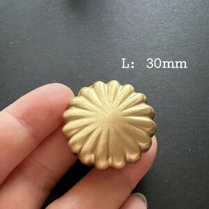 Puede incluir: Un pomo de metal de color dorado con un dise&ntilde;o decorativo en forma de sol. L: 30 mm.