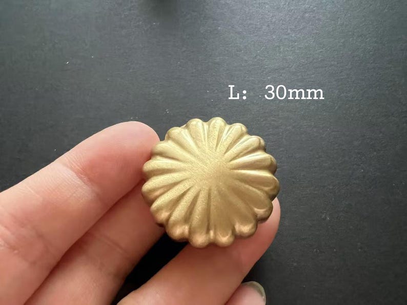 Puede incluir: Un pomo de metal de color dorado con un dise&ntilde;o decorativo en forma de sol. L: 30 mm.