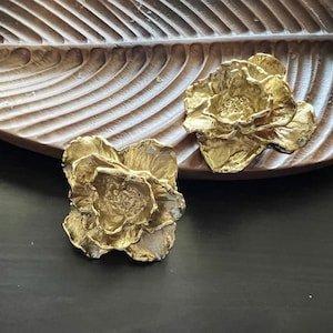 以下が含まれることがあります： 木製の表面に置かれた、金色の金属製の装飾的な花の形をした2つのピース