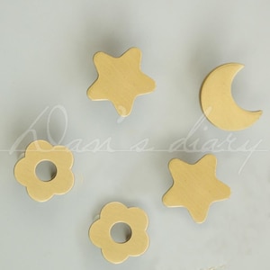 May include: Five wooden knobs in the shapes of a star, flower, moon, and two more stars. The knobs are a light yellow colour.