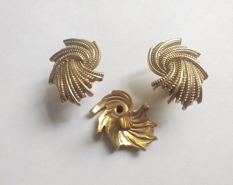 K&ouml;nnte beinhalten: Drei goldfarbene, spiralf&ouml;rmige Schrankkn&ouml;pfe. Die Kn&ouml;pfe haben ein strukturiertes, geriffeltes Design und ein zentrales Schraubenloch zur Befestigung. Die Hardware ist wahrscheinlich f&uuml;r M&ouml;bel oder dekorative Zwecke bestimmt.