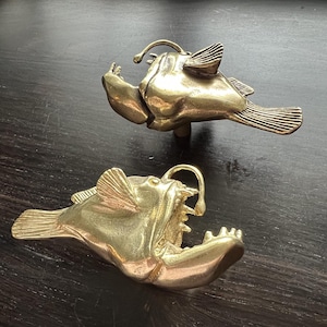 May include: Two gold-colored anglerfish sculptures. The sculptures are detailed and realistic, with open mouths and fins.