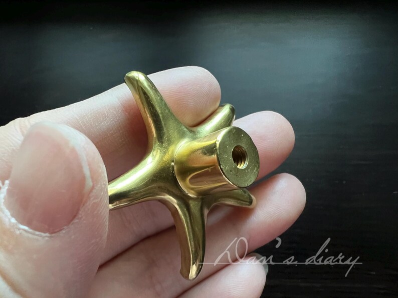 May include: Gold-toned metal cabinet knob shaped like a starfish with a threaded hole in the centre.