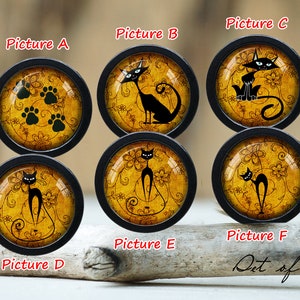 May include: Set of six black and yellow round glass cabochons with black cat designs. The cabochons are set in black metal frames. The designs include a cat with paw prints, a cat with a curled tail, a cat with a straight tail, and a cat with a long tail.